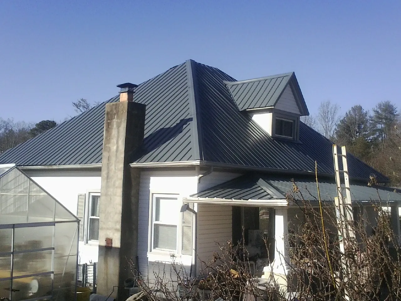 Dark blue standing seam metal roof on a white farmhouse with dormer — Slate & Tile Roof Repair by Roofing Brothers in Genoa City