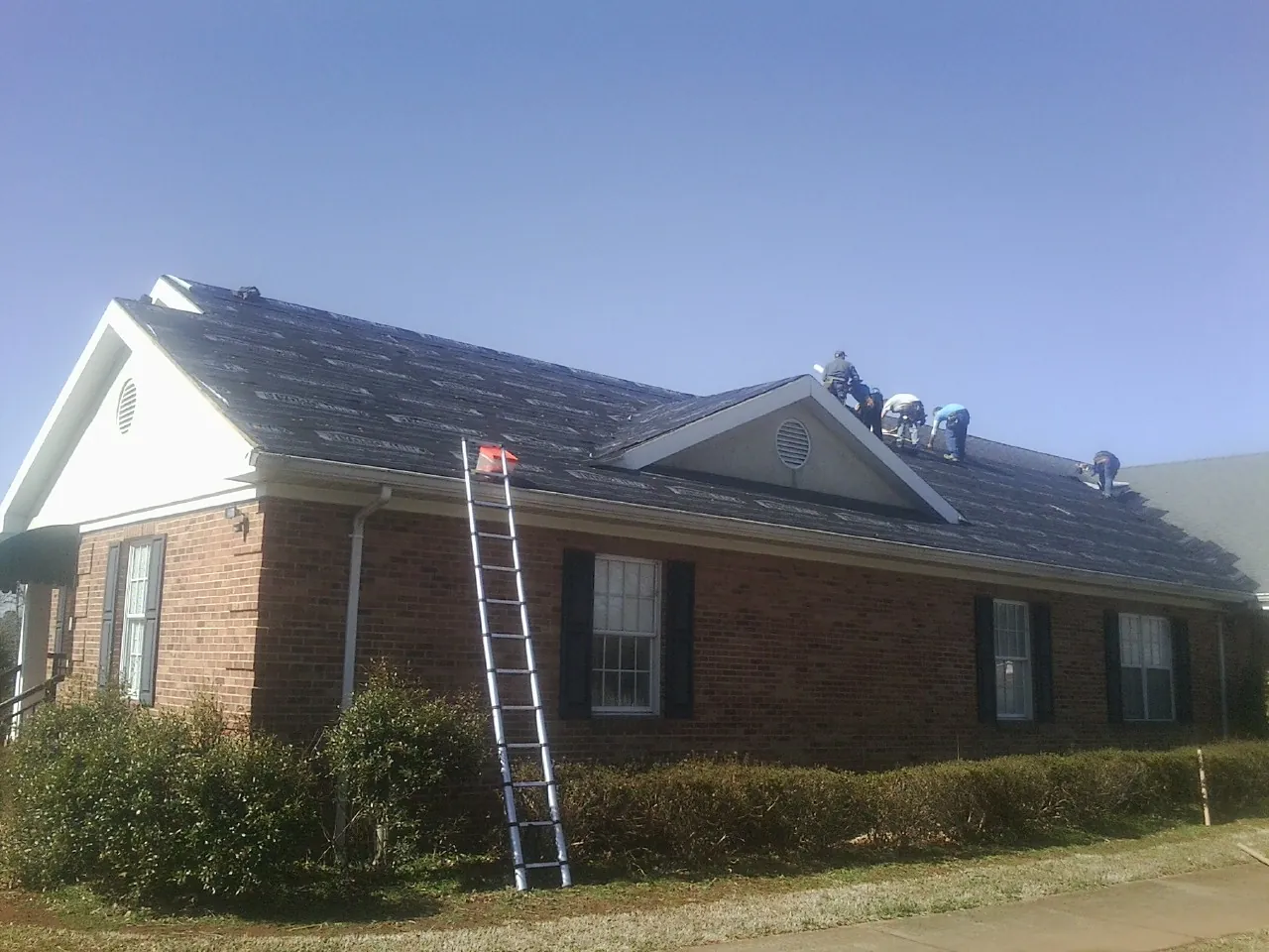 Crew tearing shingles off a brick ranch roof with a ladder set — Emergency Roof Repair work by our crew in Genoa City