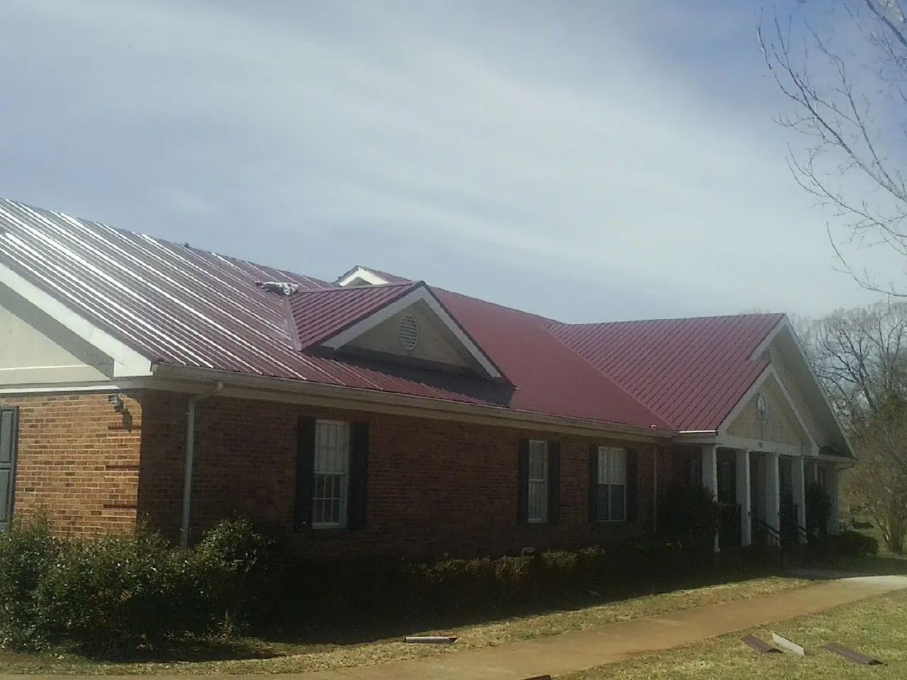 Red metal roof with gabled entries on a long brick building, from a Hail Damage Roof Repair job in Genoa City