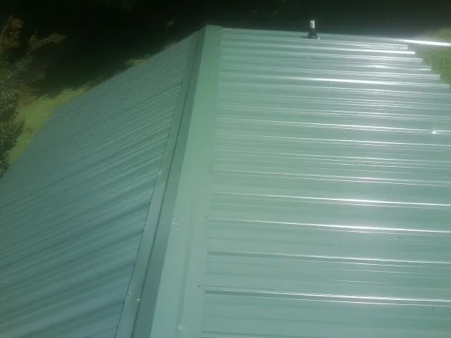 New green metal panels meeting at the ridge of a roof — Flat Roof Repair work by our crew in Genoa City
