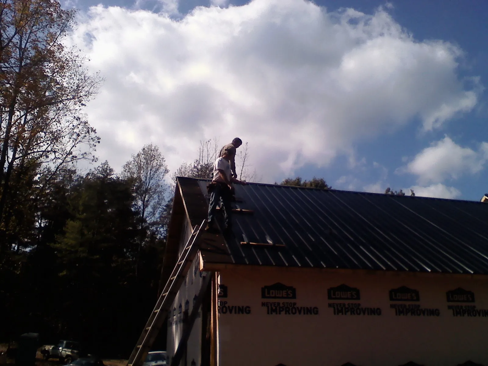 Roofer fastening dark metal panels high against a cloudy sky, from a Roof Inspection job in Genoa City