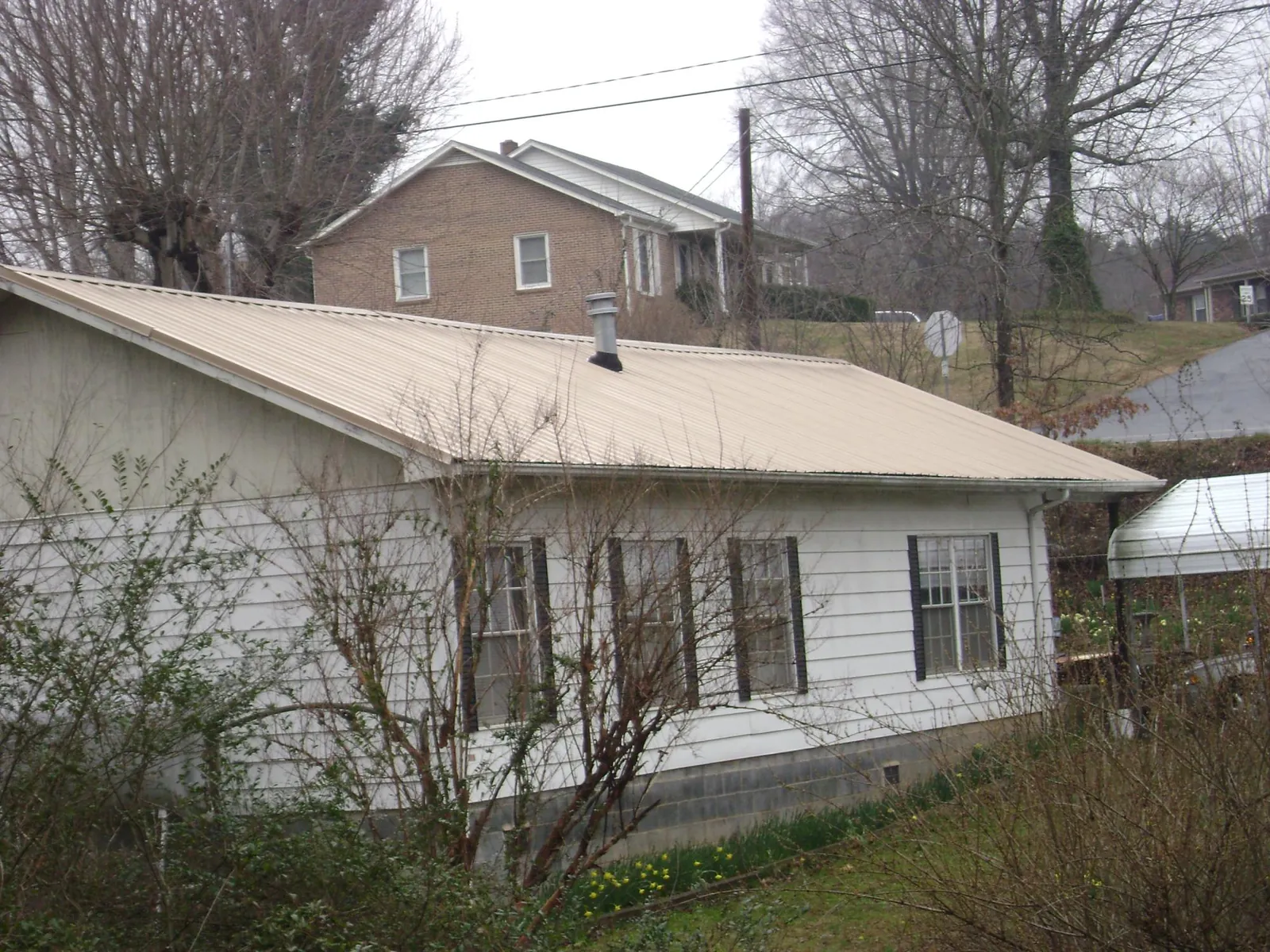 Tan metal roof on a white sided house set into a hillside — Commercial Roofing by Roofing Brothers in Genoa City